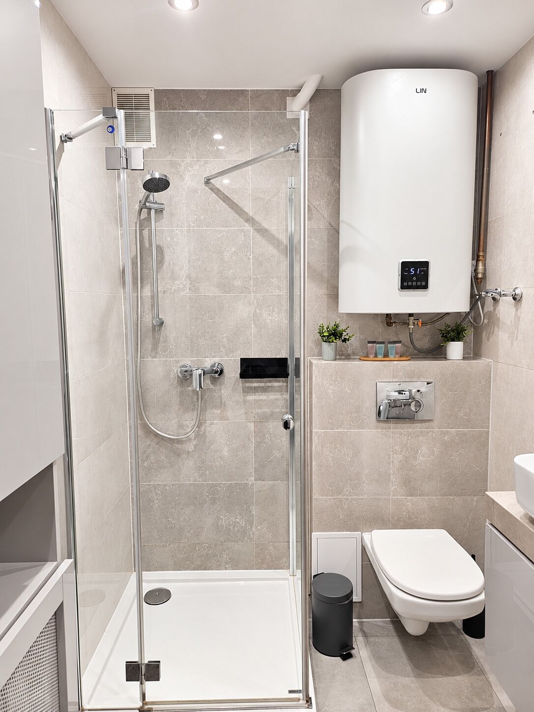 Ein modernes Badezimmer mit einer glasumrandeten Dusche, Toilette und einem eingebauten Warmwasserbereiter.