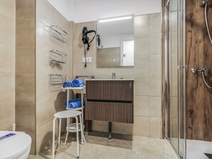 Ein Badezimmer mit Toilette, Waschbecken mit Spiegel, Duschbereich und Handtuchhalter.