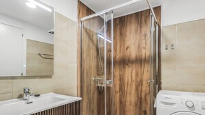 A modern bathroom with a glass-enclosed shower, a sink with a mirror, and a washing machine.