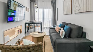 A modern living room with a grey sofa, a dining table, and a TV mounted on the wall.