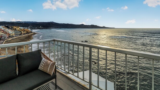 A balcony with a sofa and a view of the sea and a coastal town.