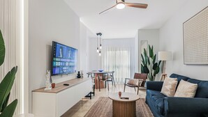 A modern living room with a flat-screen TV, a ceiling fan, a blue sofa, and a dining area with a table and chairs.