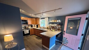 A modern kitchen with wooden cabinets, a central island, and a pink door. - Cozy Cottage in the City (Saint Ann)