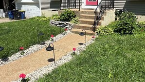 A residential house with a red door, a garage, and a well-maintained garden with a gravel path and flower beds. - Cozy Cottage in the City (Saint Ann)