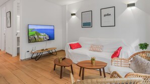 A modern living room with a white sofa, a wooden coffee table, and a TV mounted on the wall.