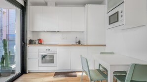 A modern kitchen with white cabinets, a built-in oven, and a microwave. There is a dining area with a table and chairs.