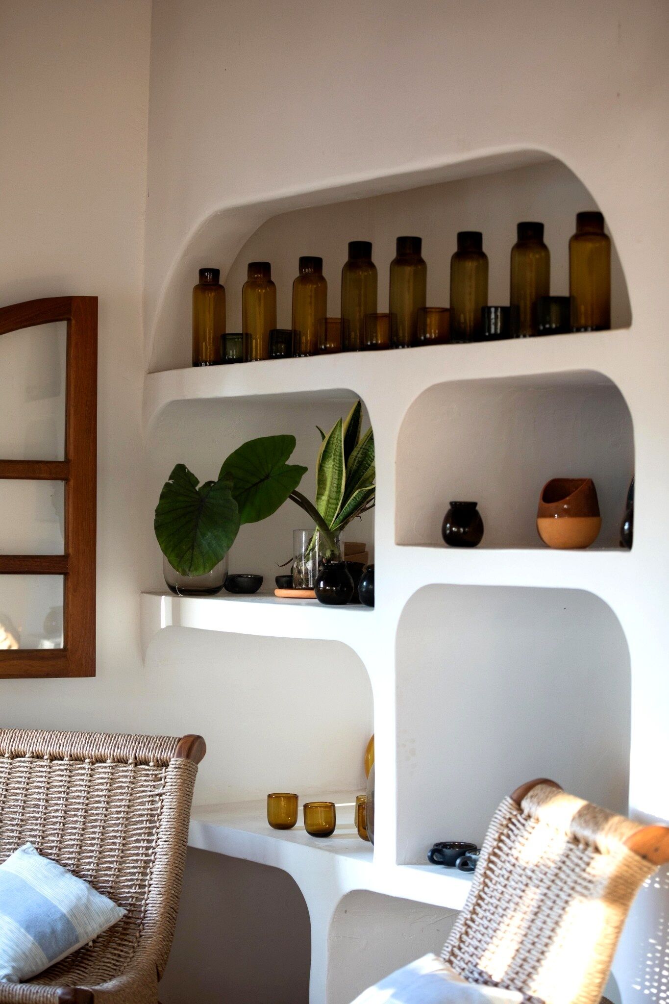 A room with wicker chairs, a shelf with bottles, a plant, and a mirror.