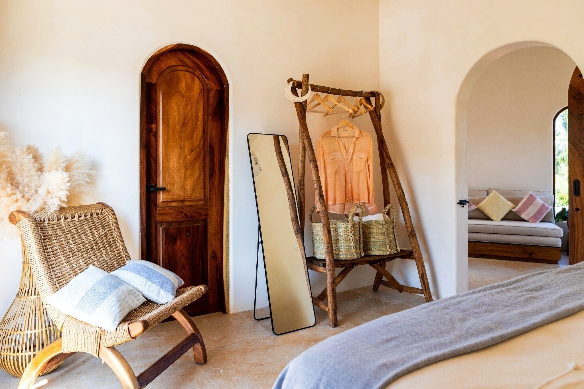 A room with a wicker chair, a wooden door, a mirror, a hanging chair, and a sofa with cushions.