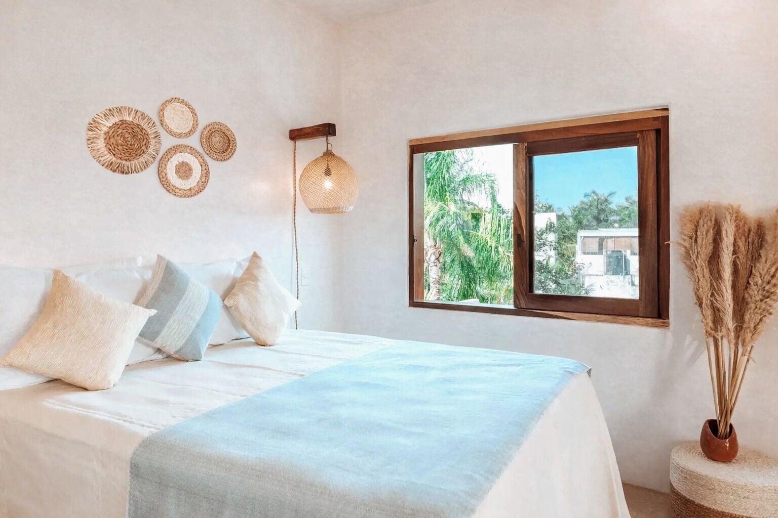 Une chambre à coucher avec un lit, des oreillers, un luminaire suspendu, une fenêtre donnant sur un beau paysage et des œuvres d’art décoratives au mur.