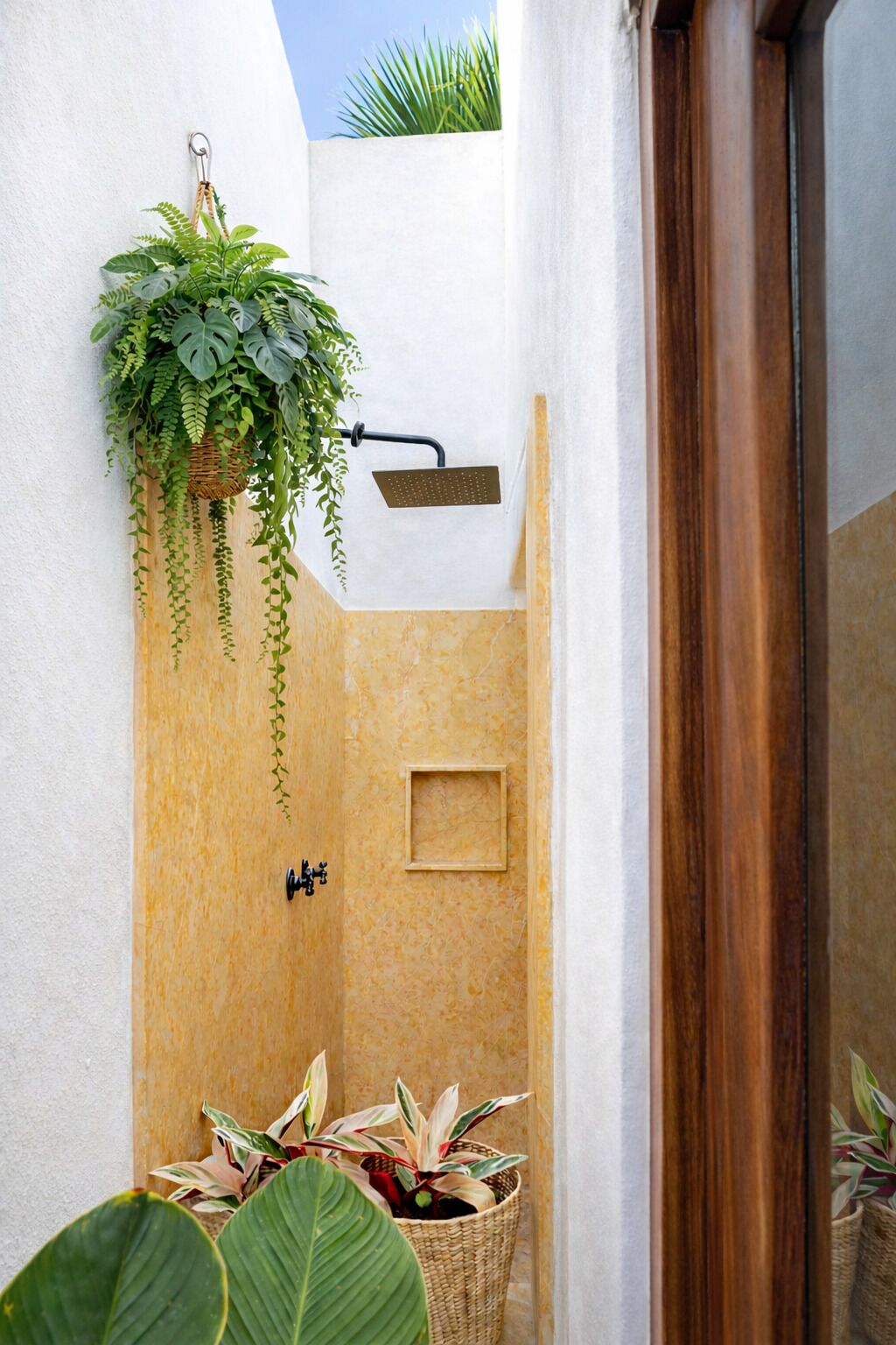 A small, enclosed shower area with a hanging plant, a showerhead, and a wall-mounted faucet.