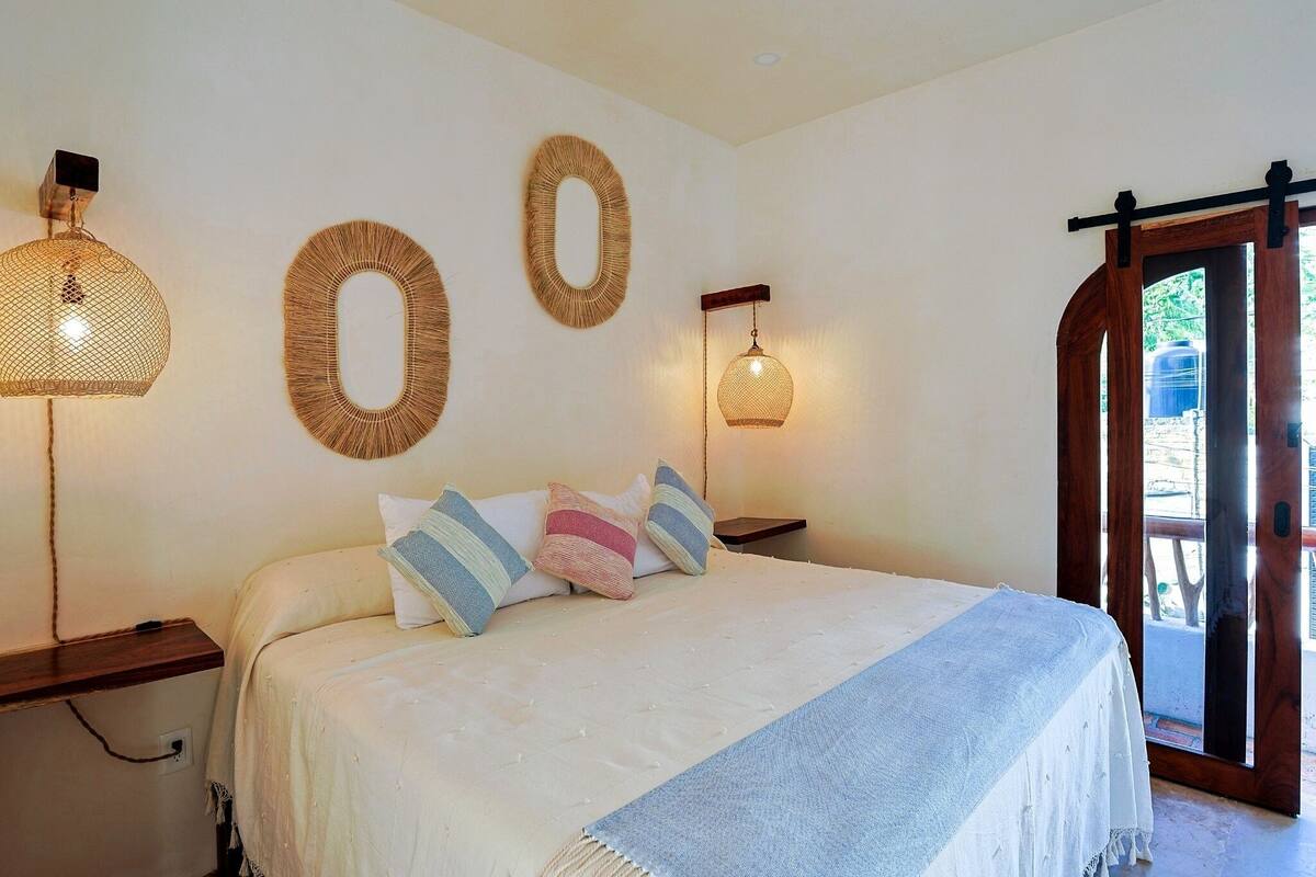 Un dormitorio con una cama, dos mesitas de noche y tres lámparas fijadas a la pared.