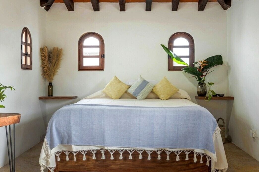A bedroom with a bed, two windows, and a plant.