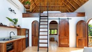 A kitchen with a central island, wooden cabinets, a built-in oven, and a ceiling fan. There are two wooden doors and a window with a view of greenery. - Amari Boutique Hotel Sayulita (Sayulita)