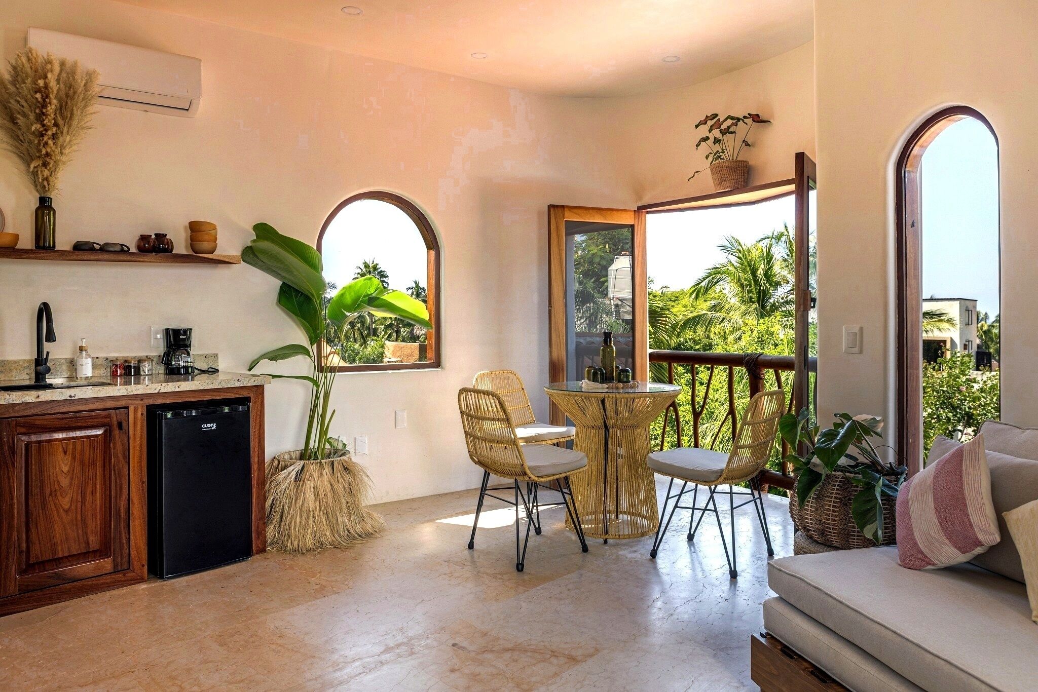 Una cocina moderna con lavavajillas incorporado, un comedor con sillas de mimbre y un amplio ventanal con vistas a palmeras.
