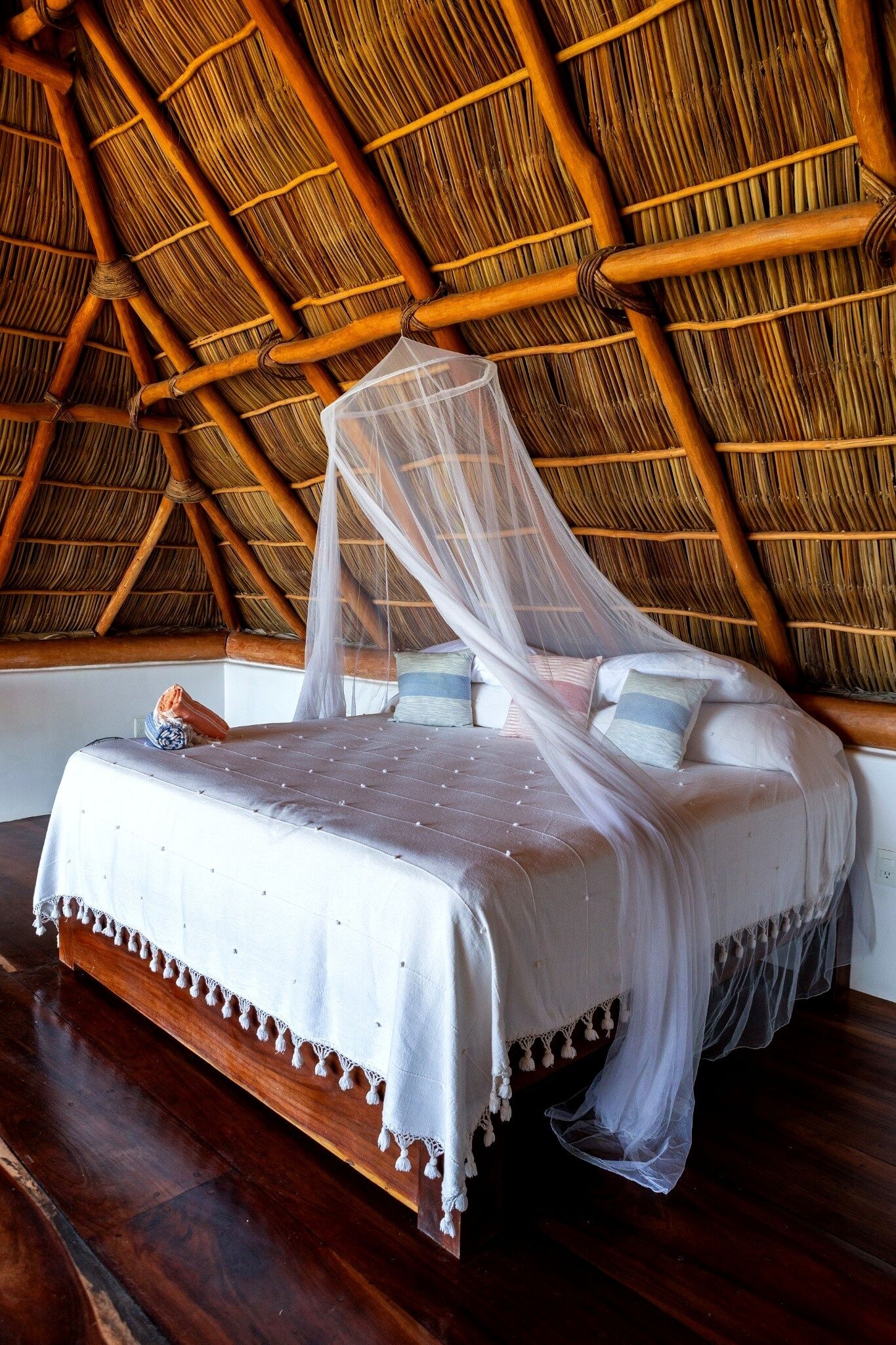 A bed with a canopy in a room with a thatched roof.