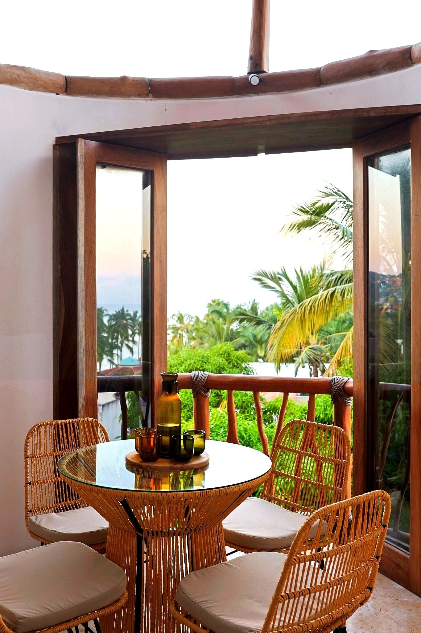 A glass-top table with wicker chairs and a view of palm trees through large windows.