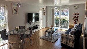 Una sala moderna con televisión de pantalla plana, mesa de comedor, sillas, un sofá y un ventanal con vistas a la calle.