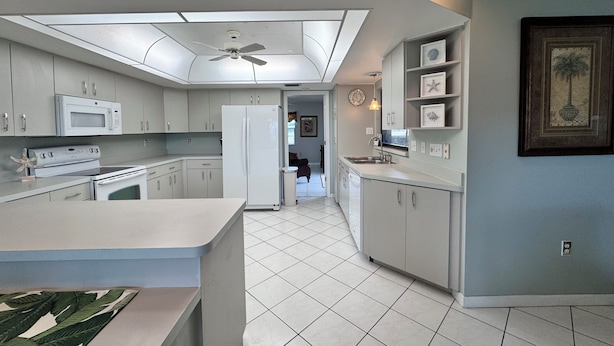 Une cuisine moderne avec des appareils électroménagers blancs, un îlot central et un ventilateur de plafond.