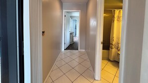 Un couloir au sol carrelé qui mène à une salle de bain avec un rideau de douche jaune.
