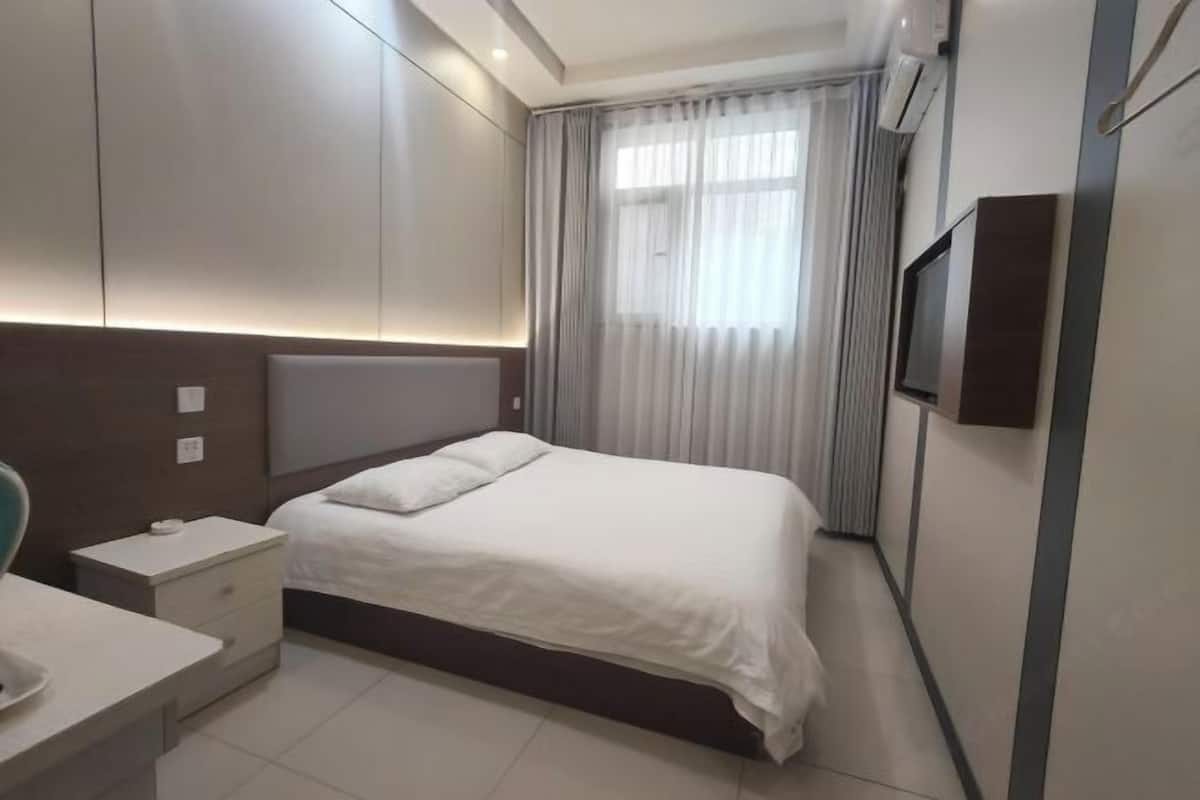 A modern hotel room with a bed, bedside table, and a television mounted on the wall.