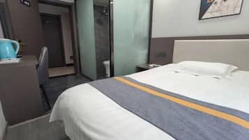 A hotel room with a bed, a desk, a chair, a coffee maker, and a shower area.