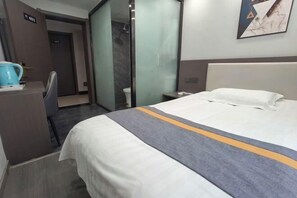 A hotel room with a bed, a desk, a chair, a coffee maker, and a shower area. - Shijiazhuang Yiguang Hotel (Shijiazhuang)