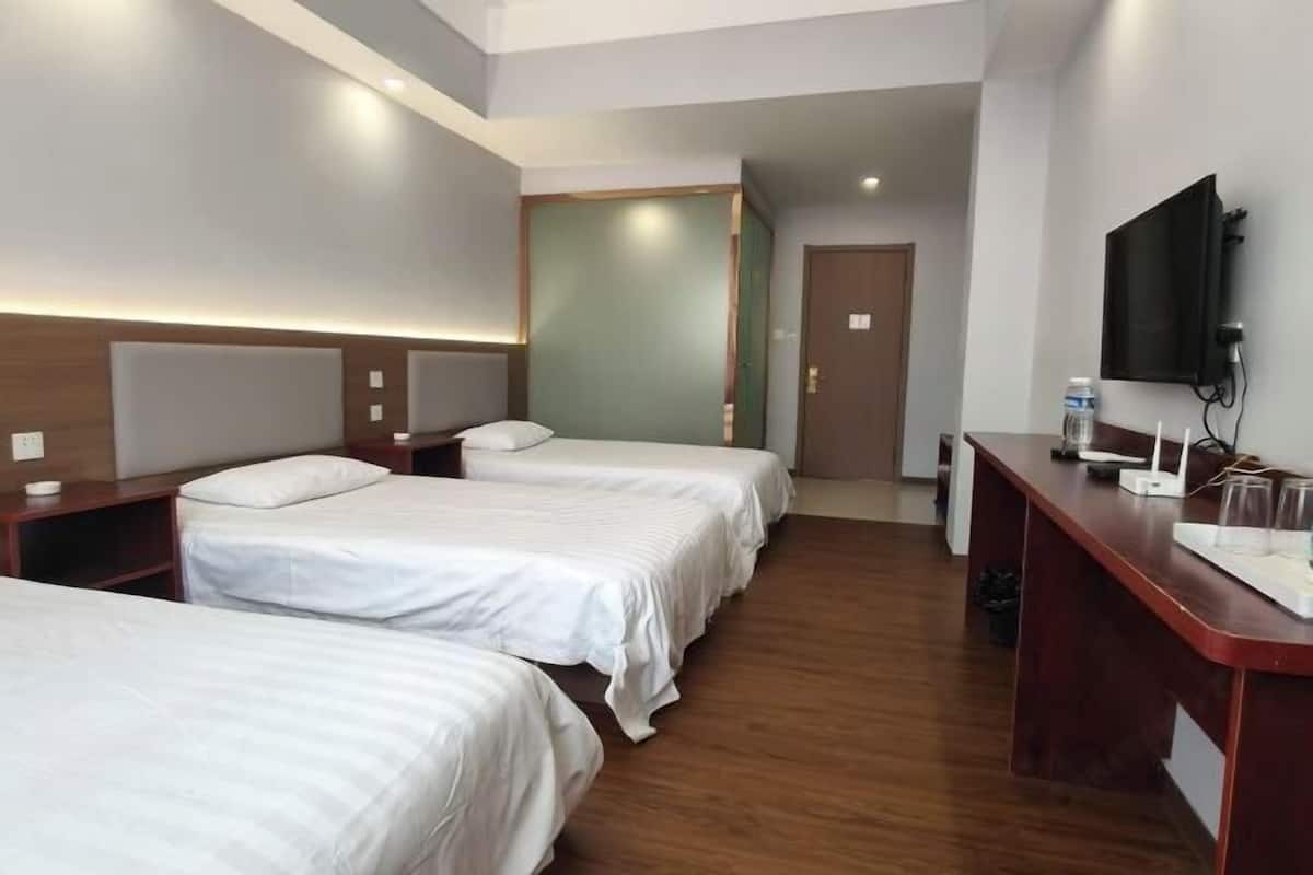 A hotel room with three beds, a desk with a TV, and a wooden floor.