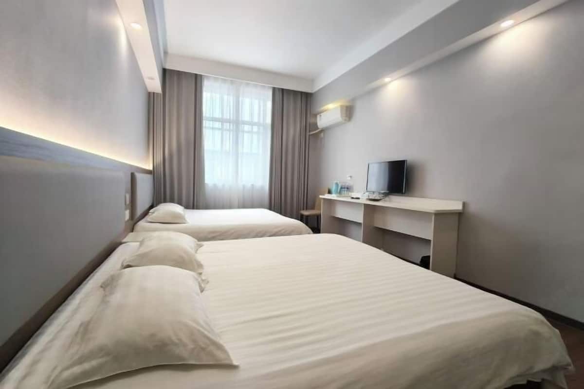 A hotel room with two beds, a desk with a TV, and a window with curtains.
