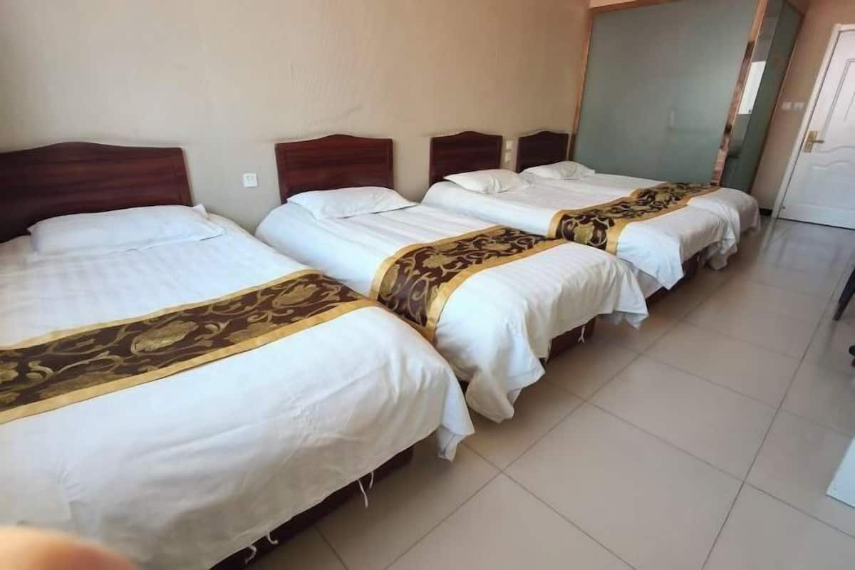 A hotel room with three beds aligned in a row, each with a wooden headboard and white bedding.