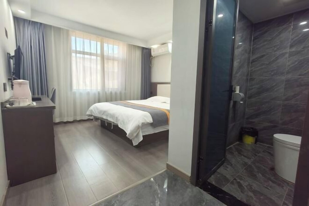 A hotel room with a bed, a desk, a shower area, and a bathroom.