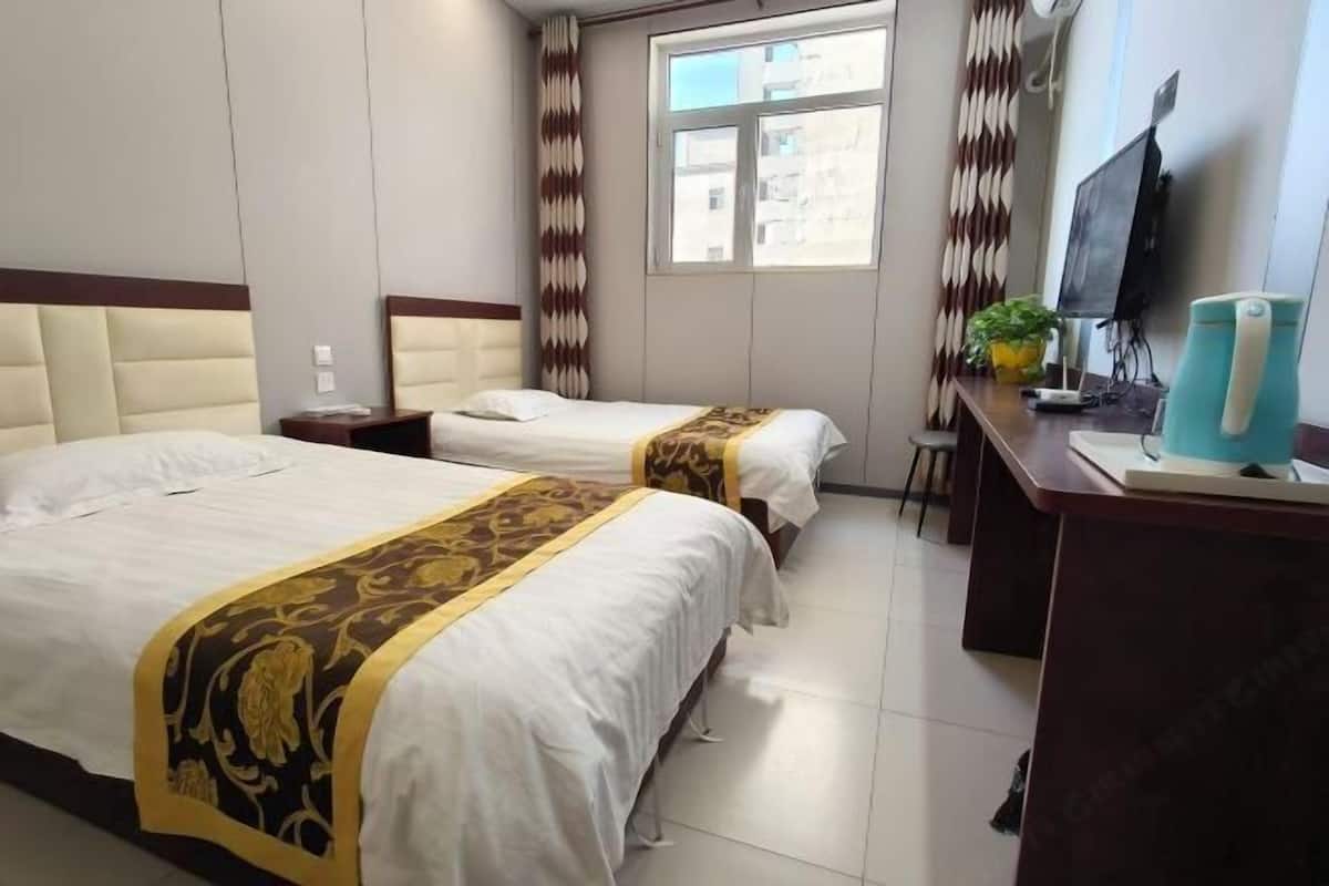 A hotel room with two beds, a desk with a computer, a TV, and a window with curtains.