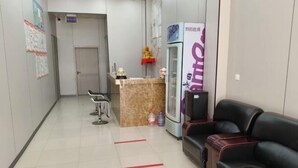 A reception area with a reception desk, a waiting area with a black leather couch, a refrigerator, and a door leading to another room. - Shijiazhuang Yiguang Hotel (Shijiazhuang)