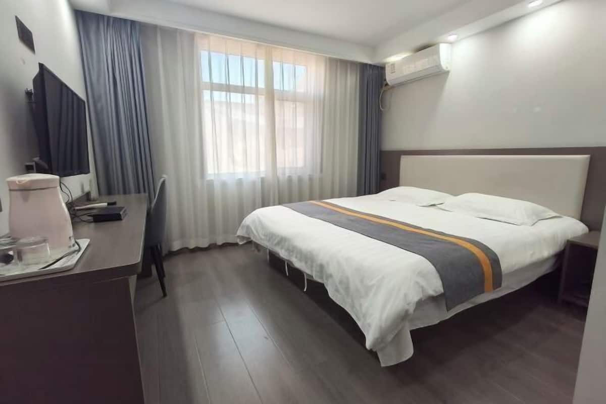 A hotel room with a bed, a desk, a chair, a TV, and a window with curtains.