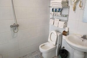 A small bathroom with a toilet, a sink, a shower, and shelves with toiletries. - Shijiazhuang Yiguang Hotel (Shijiazhuang)