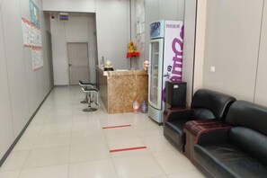 A reception area with a reception desk, a refrigerator, a black leather couch, and a chair. - Shijiazhuang Yiguang Hotel (Shijiazhuang)