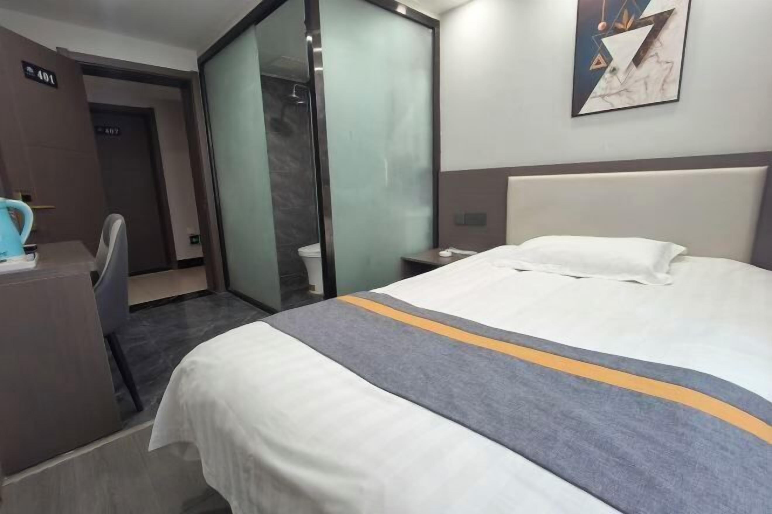 Habitación de hotel con cama, escritorio, silla, separador de vidrio y un cuadro en la pared.
