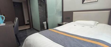 A hotel room with a bed, a desk, a chair, a glass partition, and a painting on the wall.