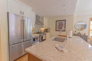 A modern kitchen with stainless steel appliances, a marble countertop, and a large window.
