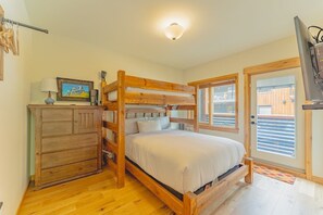 A bunk bed with a wooden headboard, a dresser with multiple drawers, a framed picture on the dresser, and a television on a stand. - Luxury Corner Condo w/ Mountain Views + Hot Tub (Canmore)