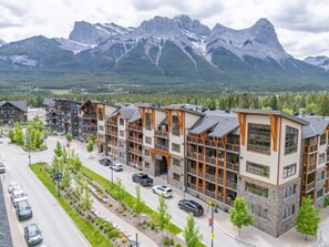 A multi-story hotel with a modern design, featuring balconies and large windows, situated in a mountainous area with a view of the peaks.