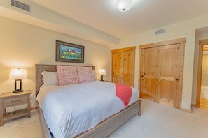A bedroom with a bed, two bedside tables, a nightstand, a painting on the wall, and wooden doors.