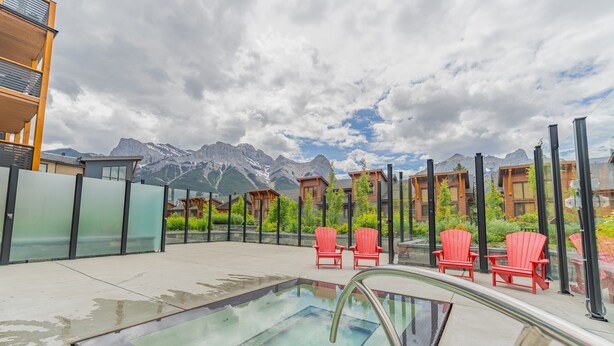 A rooftop pool area with red chairs, a glass barrier, and mountain views. - Luxury Corner Condo w/ Mountain Views + Hot Tub (Canmore)