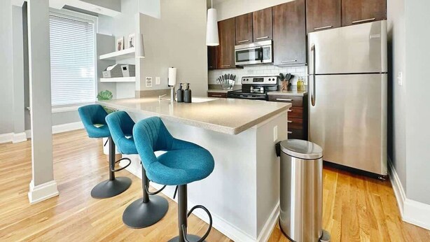 A modern kitchen with a central island, stainless steel appliances, and blue bar stools. - Boho Studio Loft in OTR Near Downtown Cincy (Cincinnati)