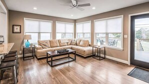 Un salon spacieux avec un canapé d’angle, une table basse et un ventilateur de plafond.
