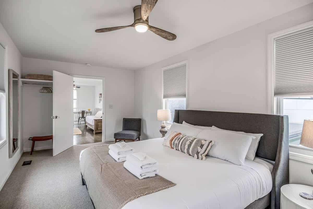 Une chambre à coucher avec un grand lit, un ventilateur de plafond, une table de chevet et une fenêtre avec des stores.