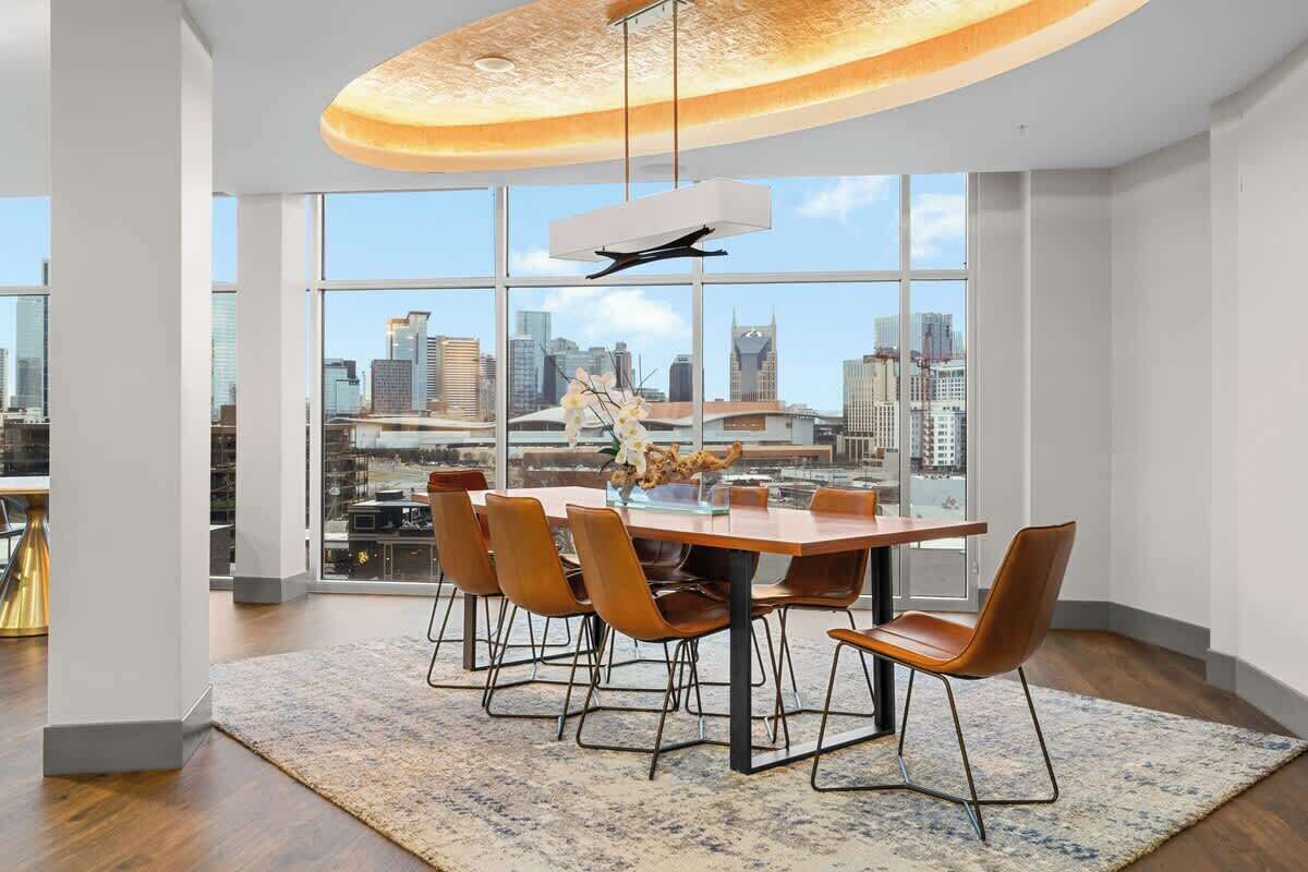 Un espace de restauration moderne, doté d’une grande table, de chaises et offrant une vue sur la ville grâce à de larges fenêtres.