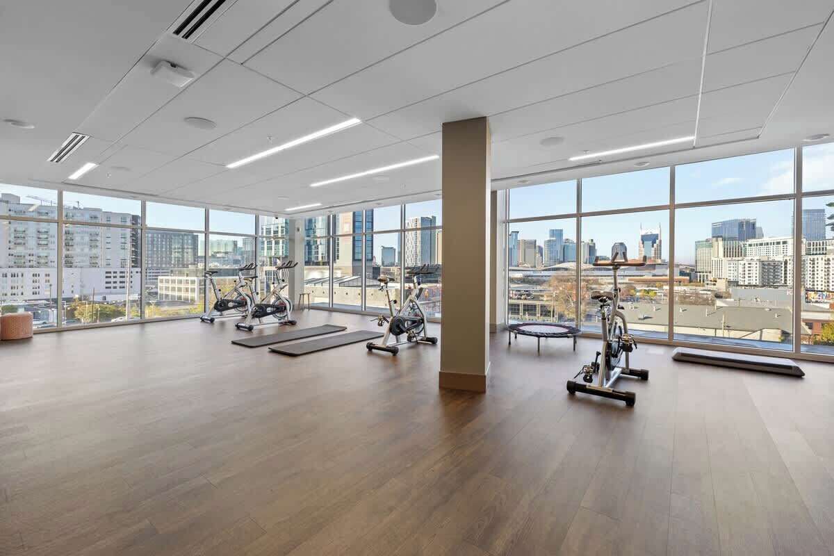 Une salle de sport spacieuse, dotée de grandes fenêtres, d’équipements d’exercice et offrant une vue sur la ville.
