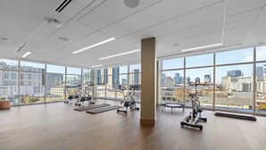 A spacious gym with large windows, exercise equipment, and a city view.