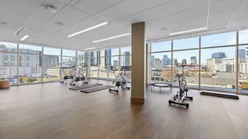 Une salle de sport spacieuse, dotée de grandes fenêtres, d’équipements d’exercice et offrant une vue sur la ville.