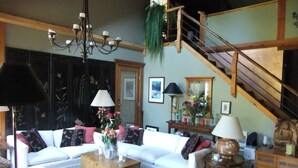 A spacious living room with a white sofa, wooden coffee table, and a staircase leading to an upper level. - Roberts Creek: Charming 3-bedroom/2 bath post 'n beam steps to Henderson Beach (Roberts Creek)